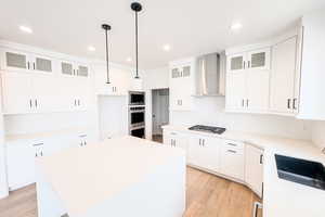 Kitchen featuring wall chimney exhaust hood, a kitchen island, glass insert cabinets, and white cabinets