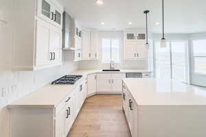 Kitchen with white cabinets, wall chimney exhaust hood, glass insert cabinets, light countertops, and a sink