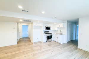 Kitchen featuring light countertops, white cabinetry, a sink, and stainless steel gas range oven