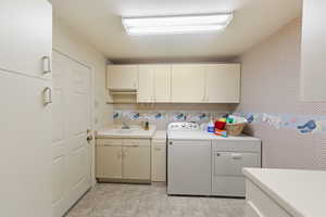 Laundry area with a sink, washing machine and dryer, cabinet space, and wallpapered walls