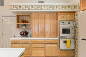 Kitchen featuring tile counters, white appliances, visible vents, and light brown cabinets