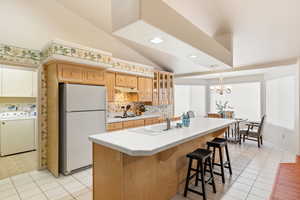 Kitchen with lofted ceiling, an island with sink, glass insert cabinets, washer / clothes dryer, and freestanding refrigerator