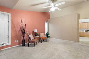 Living area with light carpet, ceiling fan, vaulted ceiling, and baseboards