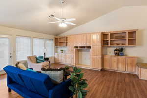 Living room with dark wood-type flooring, lofted ceiling, visible vents, and a ceiling fan