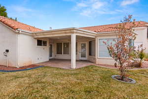 Rear view of property with stucco siding, a tiled roof, a lawn, and a patio