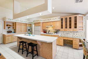 Kitchen with white appliances, a center island with sink, glass insert cabinets, light countertops, and open shelves