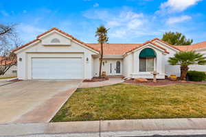 Mediterranean / spanish-style house with a garage, concrete driveway, a tiled roof, a front lawn, and stucco siding