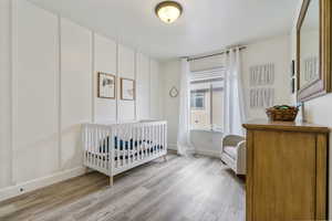 Bedroom with a nursery area, light wood-style flooring, and baseboards