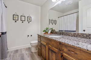 Bathroom featuring visible vents, toilet, vanity, wood finished floors, and baseboards