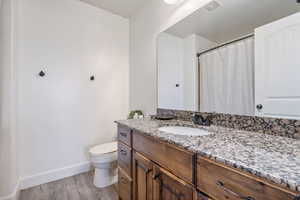 Bathroom featuring toilet, wood finished floors, vanity, visible vents, and baseboards