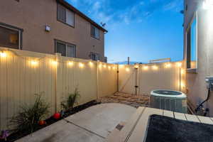 Patio terrace at dusk with a gate, a fenced backyard, and central AC unit