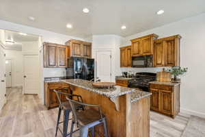 Kitchen featuring light stone counters, a center island, a breakfast bar area, brown cabinetry, and black appliances