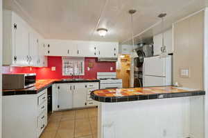 Kitchen featuring tile countertops, white appliances, sink, white cabinetry, and kitchen peninsula