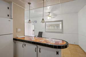 Kitchen with white cabinetry, white refrigerator, tile countertops, and hanging light fixtures