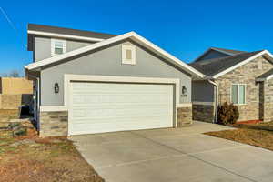 View of front facade featuring stucco siding, central AC unit, a garage, stone siding, and driveway