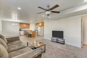 Living room featuring light carpet, ceiling fan with notable chandelier, baseboards, and recessed lighting