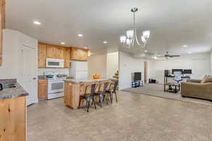 Kitchen with decorative light fixtures, a breakfast bar area, recessed lighting, open floor plan, and white appliances