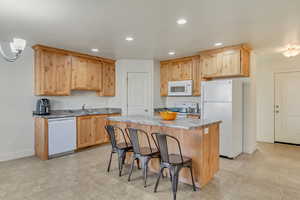 Kitchen with white appliances, light brown cabinets, a kitchen bar, and a center island