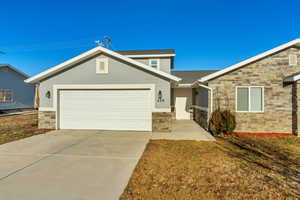 Single story home with an attached garage, concrete driveway, stone siding, stucco siding, and a front lawn