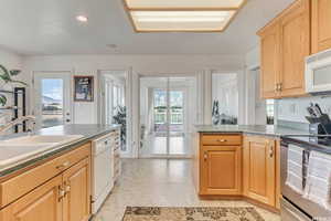 Kitchen with light floors, white appliances, a sink, light brown cabinetry, and dark countertops