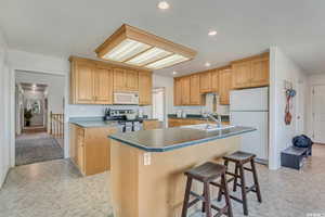 Kitchen featuring a breakfast bar area, recessed lighting, white appliances, a sink, and an island with sink