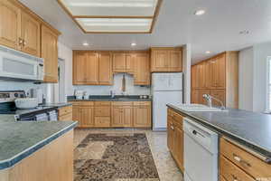 Kitchen with white appliances, dark countertops, a sink, and recessed lighting