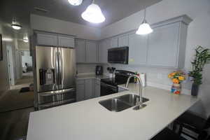 Kitchen with a breakfast bar area, stainless steel appliances, decorative light fixtures, sink, and kitchen peninsula