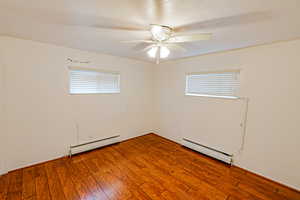 Empty room with plenty of natural light, a baseboard radiator, and wood finished floors