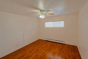 Empty room with a textured ceiling, a baseboard radiator, wood finished floors, and a ceiling fan