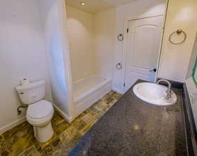 Bathroom with baseboards, toilet, shower / tub combination, stone finish floor, and vanity