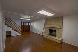 Unfurnished living room with stairway, baseboard heating, and wood finished floors