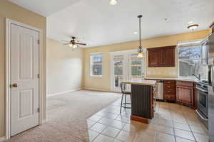 Kitchen with hanging light fixtures, a kitchen island, light carpet, stainless steel gas stove, and a kitchen bar