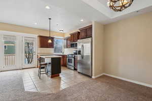 Kitchen with appliances with stainless steel finishes, a kitchen island, a kitchen breakfast bar, hanging light fixtures, and light colored carpet