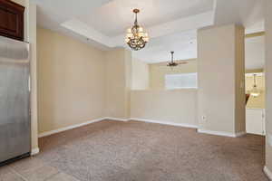 Spare room featuring light carpet, a tray ceiling, and ceiling fan with notable chandelier