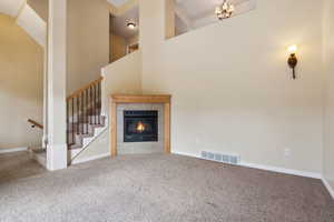 Unfurnished living room featuring a tile fireplace, carpet, an inviting chandelier, and a high ceiling