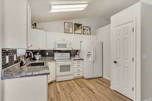 Kitchen with white appliances, decorative backsplash, white cabinets, light wood-style flooring, and a sink