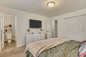 Bedroom featuring a closet, light carpet, baseboards, and ensuite bathroom