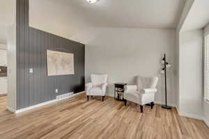 Sitting room featuring visible vents, vaulted ceiling, wooden walls, light wood-type flooring, and baseboards