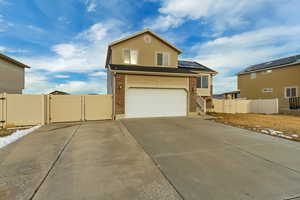 View of front facade featuring a gate, brick siding, driveway, and solar panels