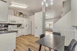 Kitchen with white appliances, white cabinets, hanging light fixtures, light wood-type flooring, and backsplash