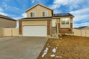 View of front facade featuring brick siding, concrete driveway, roof mounted solar panels, a gate, and fence