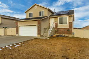 View of front of house featuring solar panels, brick siding, concrete driveway, and fence