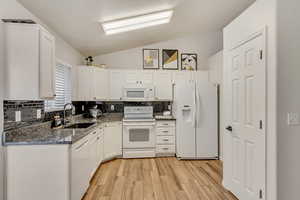 Kitchen with lofted ceiling, white appliances, white cabinetry, and a sink