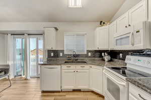 Kitchen with white appliances, white cabinetry, a sink, and dark stone countertops