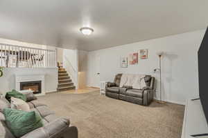 Living area with a glass covered fireplace, light colored carpet, stairway, and baseboards