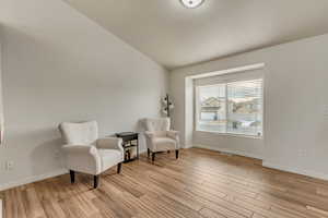 Living area with light wood-style floors, visible vents, vaulted ceiling, and baseboards