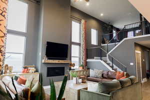 Living room with stairs, a high ceiling, wood finished floors, and a glass covered fireplace