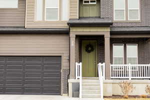 View of exterior entry with a garage, brick siding, and a shingled roof