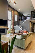 Living room with light wood-type flooring, a towering ceiling, stairway, and a fireplace