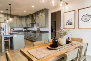 Kitchen with dark countertops, a breakfast bar area, decorative light fixtures, wall chimney range hood, and a sink